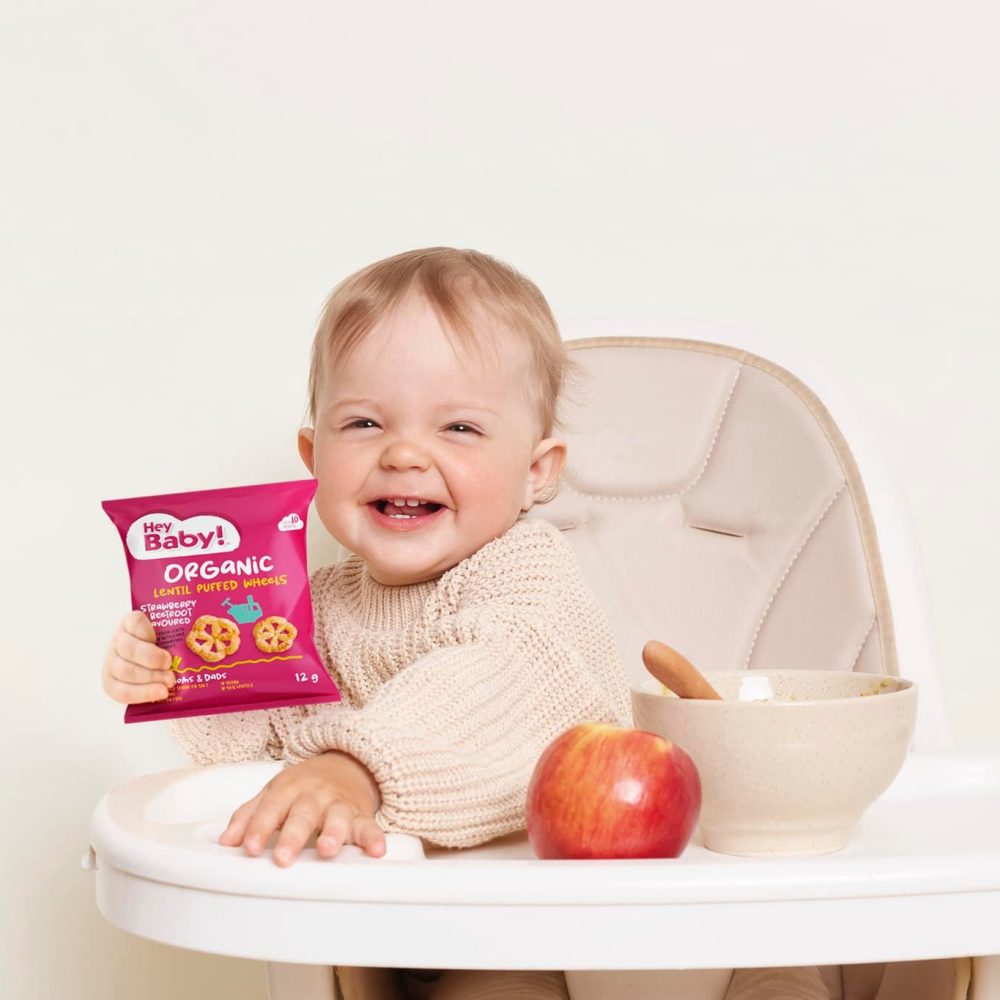 heybaby Indoor shot of smiling positive baby sitting in a chair against white isolated background, kid with water bottle and fruit having fun during breakfast or dinner.